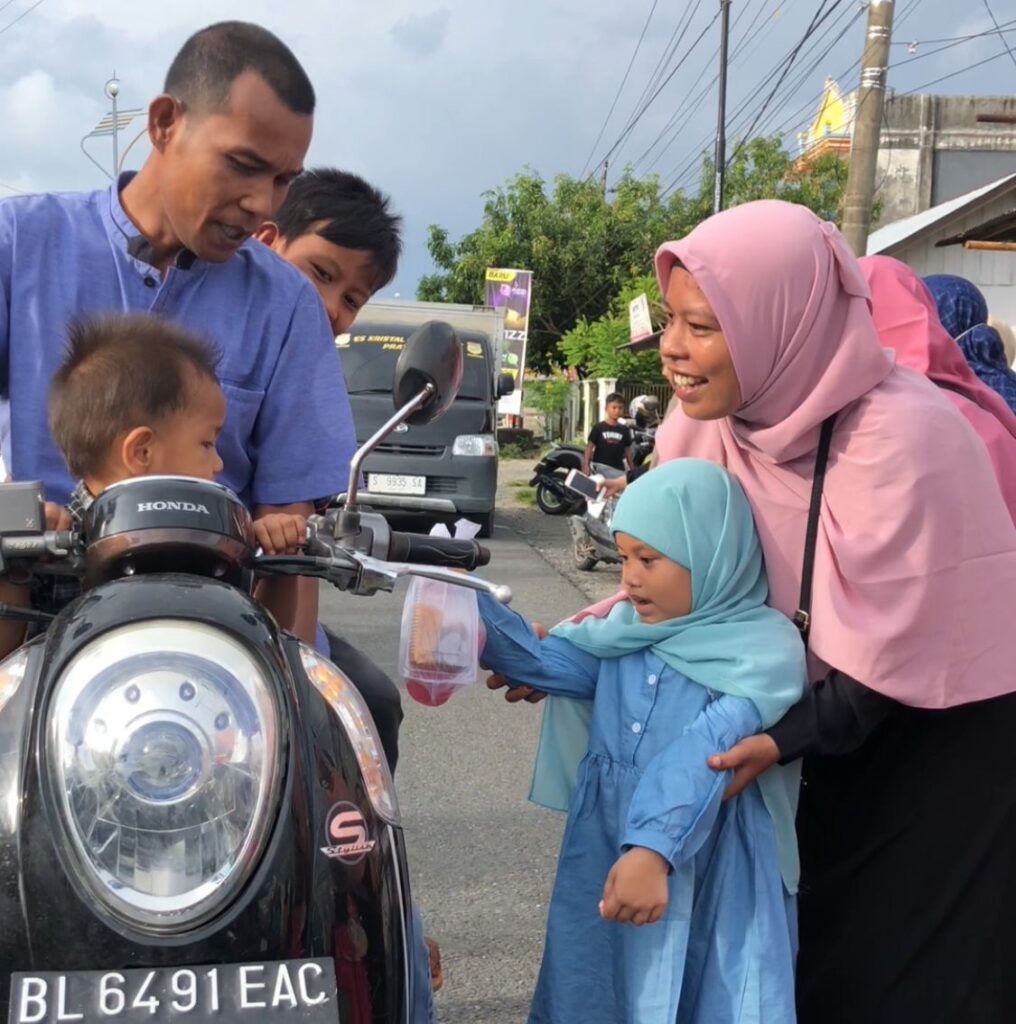 Salah seorang guru TK Az-Zahira membantu siswanya berbagi takjil kepada pengendara